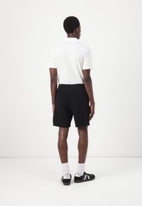 Kurzarm-weißes Poloshirt, schwarze Shorts und schwarze Sneaker mit weißen Akzenten. Eine schlichte Textur mit elastischem Bund und zwei Gesäßtaschen.