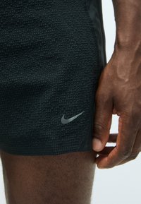 Schwarze Nike Sportshorts aus strukturiertem Stoff, mit schlankem Design und kleinem silbernen Logo an der Seite. Nahaufnahme des Materials und der Passform.