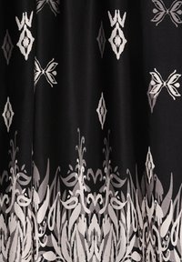 Tissu noir avec des motifs floraux et géométriques blancs symétriques, comprenant des papillons et des formes en losange, créant un design de bordure décoratif.