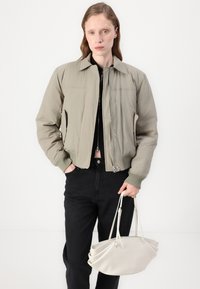 Svijetlo maslinasto zelena bomber jakna sa zatvaranjem na zip, rebrastim manžetama i bočnim džepovima. Crne traperice visokog struka i bijela torba sa strukturom.