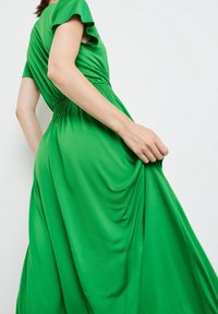 Zelené šaty s krátkým rukávem a staženým pasem a volnou sukní. Vyrobené z hladkého materiálu, mají jemné volány a pohodlný střih.