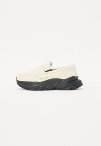 Chaussure slip-on en cuir blanc cassé avec une semelle en caoutchouc noire. Présente une forme arrondie et des accents texturés noirs pour une meilleure adhérence.