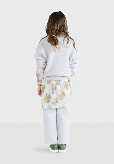 Svijetloplavi flis pulover, košulja s uzorkom životinjskih printova, svijetloplave hlače i zelene cipele s bijelim potplatima. Opušteni slojeviti outfit.