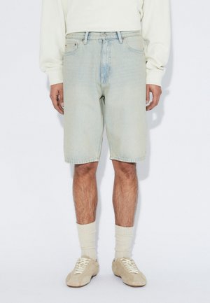 Lyseblå denimshorts med en afslappet pasform, der har et lige snit, fem-lomme-design og lynlås i skridtet. Båret med beige sko og cremefarvede sokker.