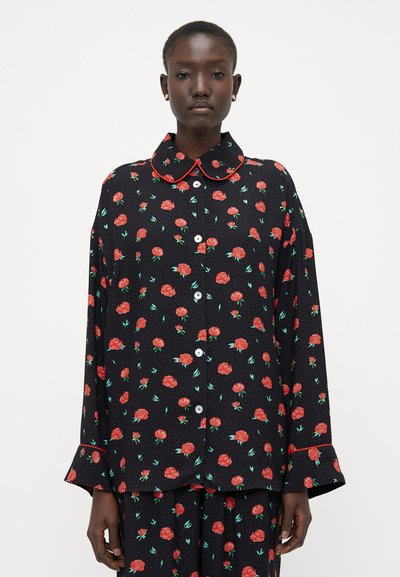 Camisa negra de flores con rosas rojas y hojas verdes, con un cuello redondeado, cierre de botones en el frente y ribete rojo en contraste a lo largo del cuello y los puños.