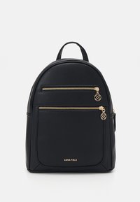 Mochila de imitación de cuero negra con forma redondeada, dos bolsillos frontales con cremallera y herrajes dorados, y un asa en la parte superior. Nombre de la marca "ANNA FIELD" en la parte frontal.