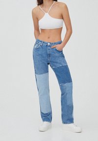 Jean patchwork en denim bleu clair avec des nuances variées, des détails usés, une coupe droite et un design classique à cinq poches.