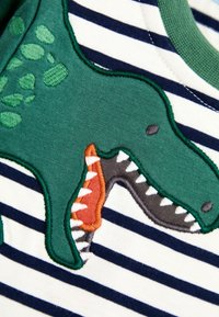 Vihreä dinosaurustikkaukset raidallisella kankaan paidassa; siinä on oranssia ja harmaata korostusta, pehmeää puuvillaa, jossa on rakenteellinen, pörröinen muotoilu.