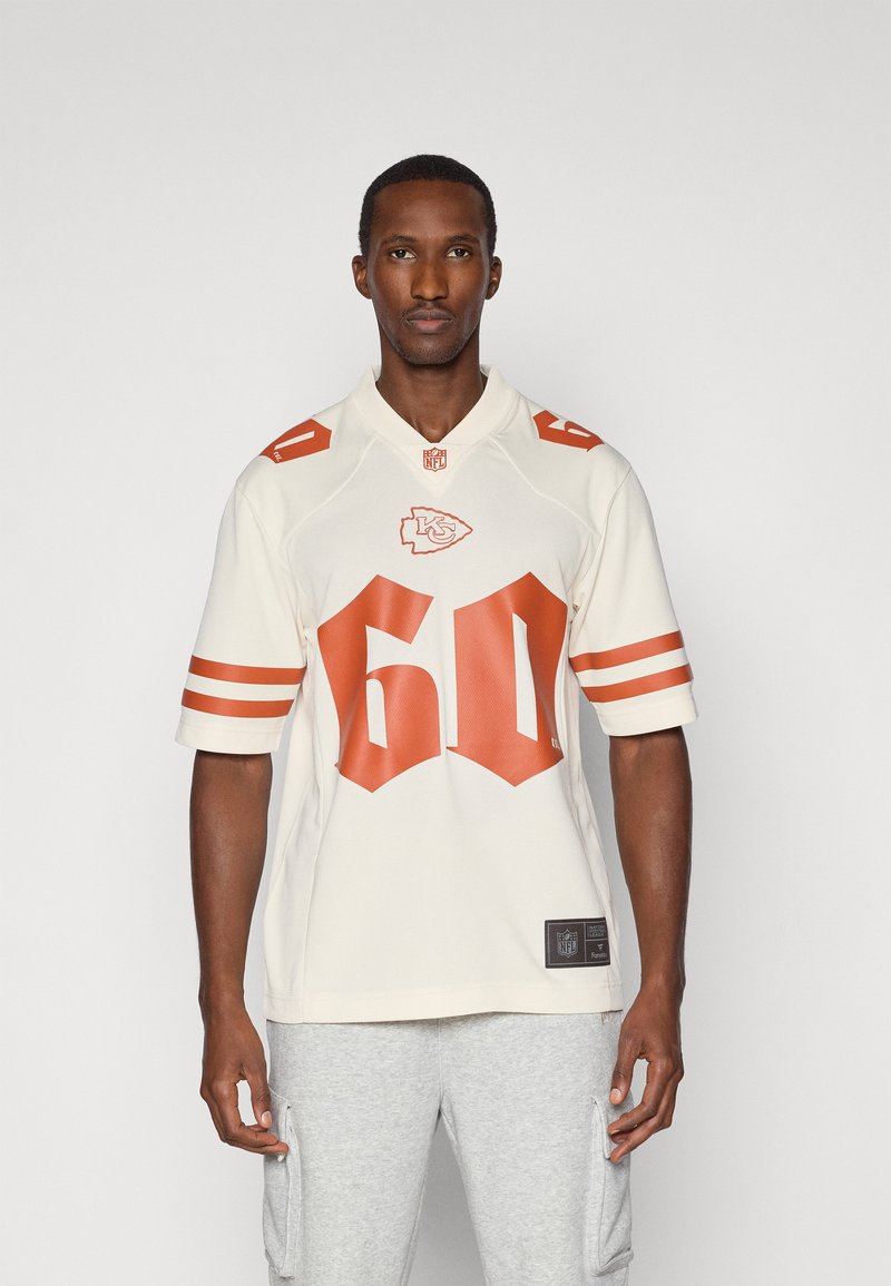 Kreemi NFL-jersey oranssilla yksityiskohdilla, jossa on suuri numero 60 ja joukkueen logo. Lyhyet hihat ja urheilukravaatti valkoisilla raidoilla.