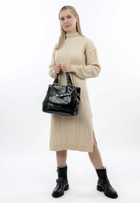Svart, strukturerad handväska med två handtag och en dekorativ sp�änne, matchad med en beige, stickad klänning med kabelmönster och svarta ankelstövlar.