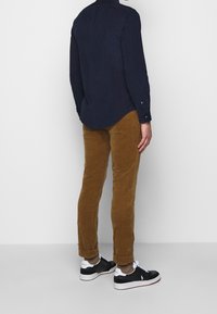 Granatowa koszula z długim rękawem, brązowe spodnie sztruksowe i czarne tenisówki z białymi detalami. Spodnie podwinięte nad kostką.