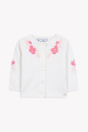 Λευκό πλεκτό ζακετάκι με κοντά μανίκια, διακοσμημένο με ροζ κεντημένα λουλουδένια μοτίβα, γιακά με κυματιστό τελείωμα και κούμπωμα με κουμπιά μπροστά.
