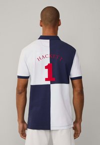 Pikétröja med delad design i marinblått och vitt, med röd "HACKETT"-logotyp och nummer "1" på baksidan. Klassisk krage och korta ärmar.