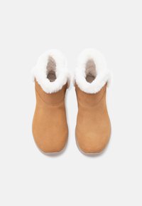 Tan-Suede-Ankelstiefel mit weißem Kunstfellfutter am Schaft, glatte Textur, runde Zehenform und einer weichen Sohle.