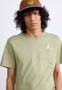 Oliven grøn T-shirt med rund hals og korte ærmer, med et hvidt Jordan-logo på venstre bryst. Brun cap med broderet logo.