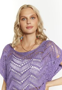 Top de ganchillo morado con un patrón de chevron, textura de tejido abierto y un escote amplio. Complementado con joyas en capas de oro.