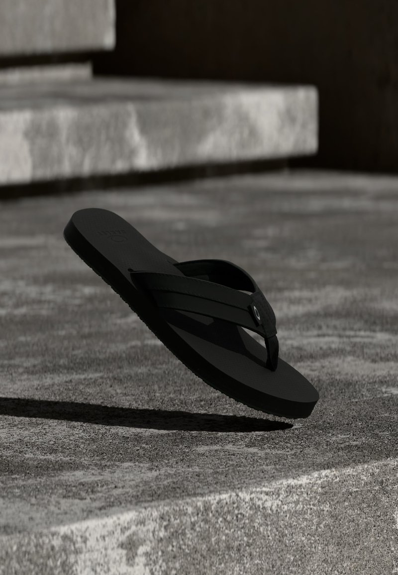 Μαύρο σανδάλι σαγιονάρας κρεμασμένο πάνω από υφή κυρτών σκάλων από σκυρόδεμα, ρίχνοντας σκιά στο έδαφος με φυσικό φωτισμό.