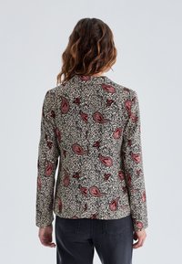 Blus med långa ärmar i krämfärgad och svart, med ett paisleymönster i röd och mörka nyanser. Mjukt tyg med en strukturerad passform.