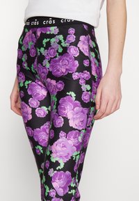 Collant con uno sfondo nero decorato da vivaci rose viola e foglie verdi. Vita elastica con dettaglio del logo. Tessuto liscio e elastico.