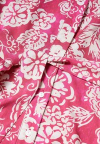 Chemise à boutons rose avec des motifs floraux abstraits blancs, en tissu léger, texture lisse, et cinq boutons blancs sur la patte de boutonnage.