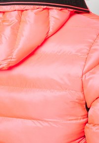 Różowa pikowana kurtka puchowa z ocieplanym kapturem i czarnym wykończeniem na kołnierzu, zbliżenie na ramię i górną część pleców.