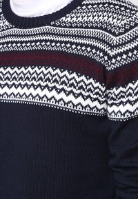 Stickad tröja i marinblått med vit och vinröd mönstrad yoke. Har en rund halsringning och strukturerad tyg. Mysigt, medelviktigt material.