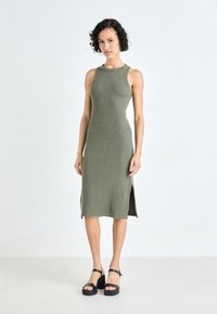 Olive green ribbed knit midi dress with sleeveless design and side slits, paired with black platform sandals featuring adjustable straps.