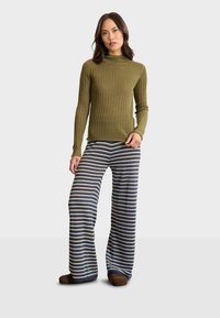 Olijvenkleurige ribbel turtleneck gecombineerd met blauw en beige gestreepte wijde pantalon. De outfit heeft een zachte textuur en een relaxte pasvorm.
