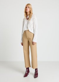 Pull en maille blanc avec un motif en losange, associé à un pantalon beige à jambes larges et des bottines bordeaux à bouts pointus.