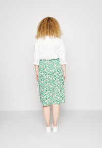 Saia verde floral com cintura ajustada e design até ao joelho, combinada com uma camisa branca de botões, com mangas até ao cotovelo.