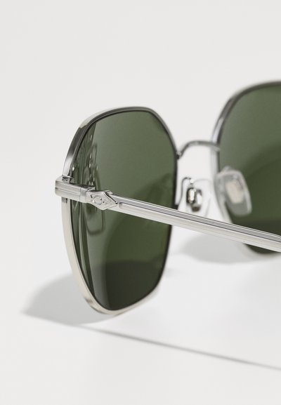 Óculos de sol metálicos com uma armação prateada, lentes verdes, forma quadrada e hastes finas e elegantes. Detalhe de hardware notável na dobradiça.