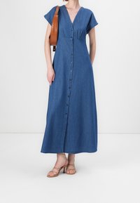 Denim-maksimekko, jossa on hihattomat hihat, V-pääntie ja etupuolella nappikiinnitys. Yksivärinen tummansininen väri, hiukan istuva vyötäröltä, löysä hame.