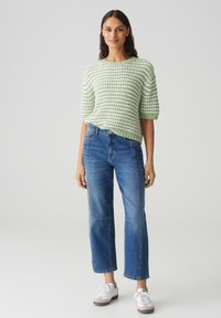 T-shirt à motifs verts et blancs en tricot avec des manches courtes, associé à un jean bleu droit et des baskets blanches. Look simple et décontracté.