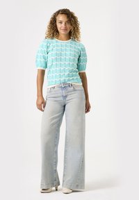 Suéter texturizado azul claro con patrones de olas blancas, combinado con jeans de pierna ancha de lavado claro y tacones de color crema.