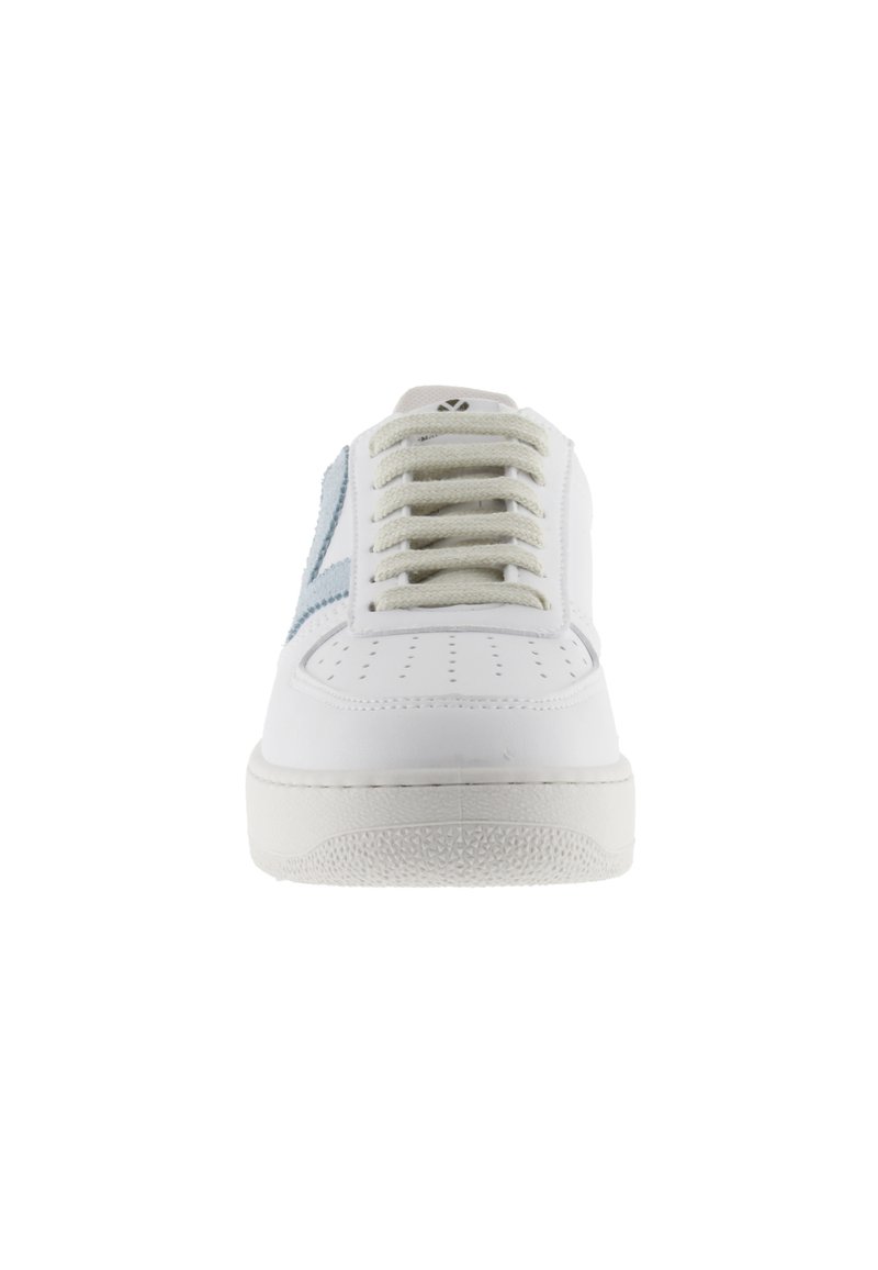 Vista frontal de una zapatilla blanca con una franja lateral azul claro, cordones blancos y suela texturizada sobre un fondo blanco.