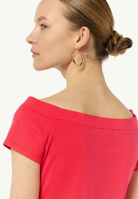Czerwona bluzka na ramiączkach z krótkim rękawem, wykonana z gładkiego materiału. Złote kolczyki w kształcie kół dopełniają stylizację, podkreślając dekolt.