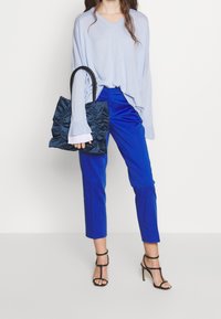 Maglione azzurro chiaro a scollo a V, pantaloni blu navy aderenti e una borsa a tracolla nera con volant. Il modello indossa tacchi neri con cinturini.