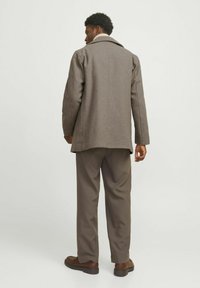 Manteau en mélange de laine marron avec un col en notch, assorti à un pantalon taupe. Le manteau a une coupe cintrée et un subtil détail texturé.