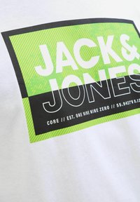 Weißes T-Shirt mit einem grafischen Design aus grünen und schwarzen Streifen. Der Text enthält "JACK & JONES" sowie zusätzliche Details in kontrastierenden Farben.