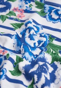 Blumenstoff mit blauen und weißen Rosen, grünen Blättern und rosa Akzenten auf einem blau-weiß gestreiften Hintergrund. Weiche Textur.