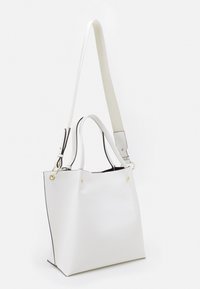 Bílá syntetická taška přes rameno se strukturovaným tvarem, s černým olemováním, odnímatelným popruhem a zlatými akcenty. Texturovaný povrch.
