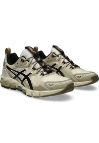 Baskets de course beige avec accents noirs, matériau texturé, tige en mesh et semelle en caoutchouc. Avec lacets noirs et logo sur la languette.