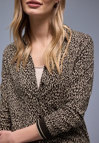 Cardigan imprimé léopard avec une fermeture boutonnée, doté d'un poignet côtelé contrastant noir et blanc. Le tissu est lisse et léger.