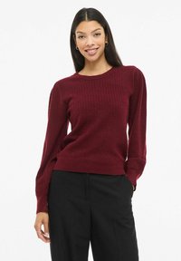 Bordowy sweter dziany z teksturowanym wzorem, okrągłym dekoltem i długimi rękawami; w połączeniu z czarnymi spodniami dla pełnego wyglądu.