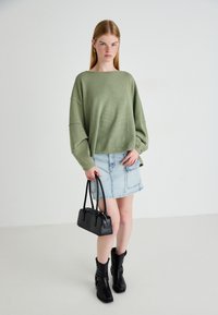 Olivenfarget oversized ribbestrikket genser, lys denim miniskjørt, svart strukturert håndveske, og kraftige svarte hæler.