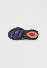 Semelle en caoutchouc noir avec des accents violets et un renfort orange au talon. Surface texturée avec différents motifs de semelle pour une meilleure adhérence.