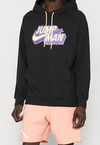 Felpa nera con grafica "JUMP MAN" in viola e giallo. Presenta una tasca frontale e stringhe con una finitura testurizzata.