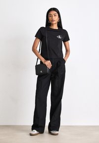 T-shirt in cotone nero con logo, abbinato a pantaloni neri a vita alta e una piccola borsa a tracolla nera. Scarpe slip-on argento.