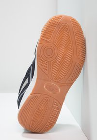 Schwarzer Sportschuh mit strukturiertem Obermaterial, ausgestattet mit einem weißen Streifenmuster und einer strapazierfähigen, orangefarbenen Gummisohle mit Traktionsmustern.