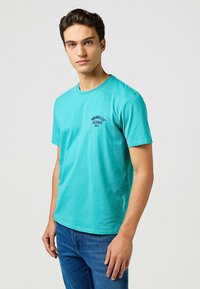 Turkoois katoenen t-shirt met korte mouwen, ronde halslijn en een lichte pasvorm. Bevat een klein marineblauw logo op de borst.